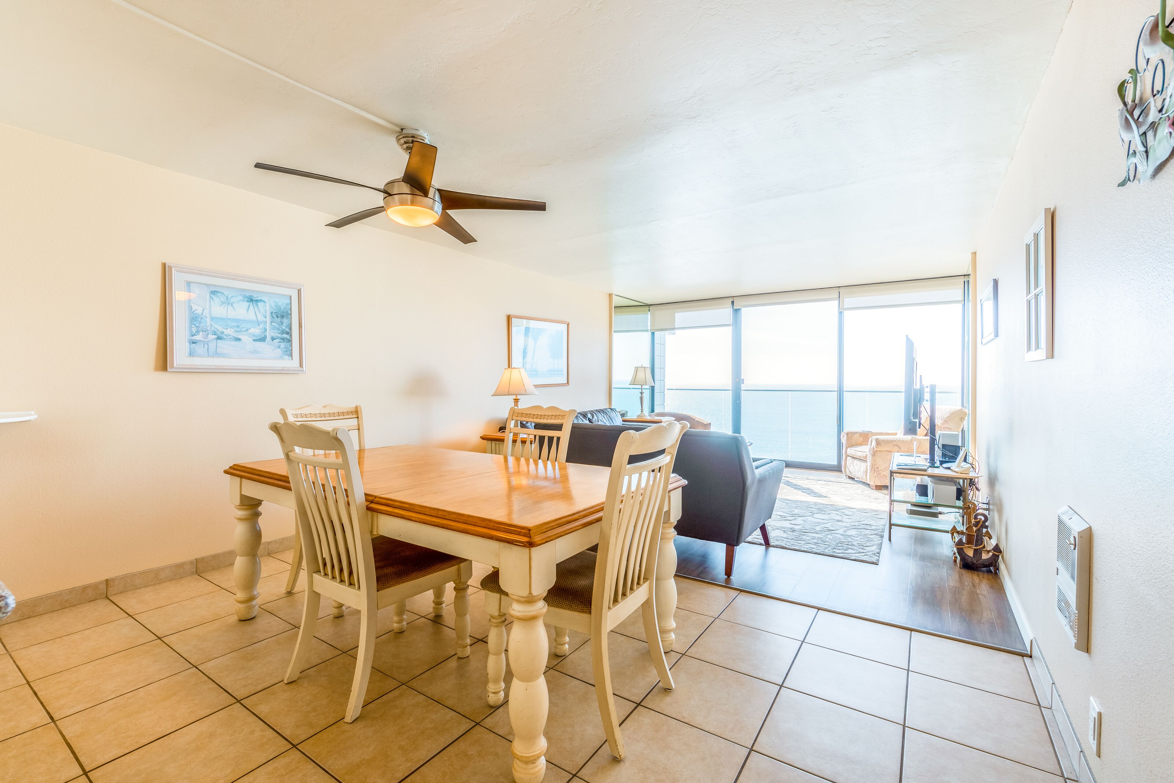 A dining area with a wooden table and chairs, a ceiling fan, and a view to the outside.