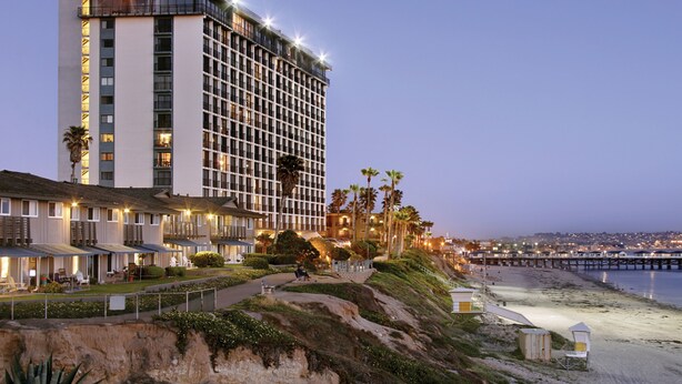 Ein Hotel an der Küste mit mehreren Etagen, Blick auf den Strand und einem Pier im Hintergrund.