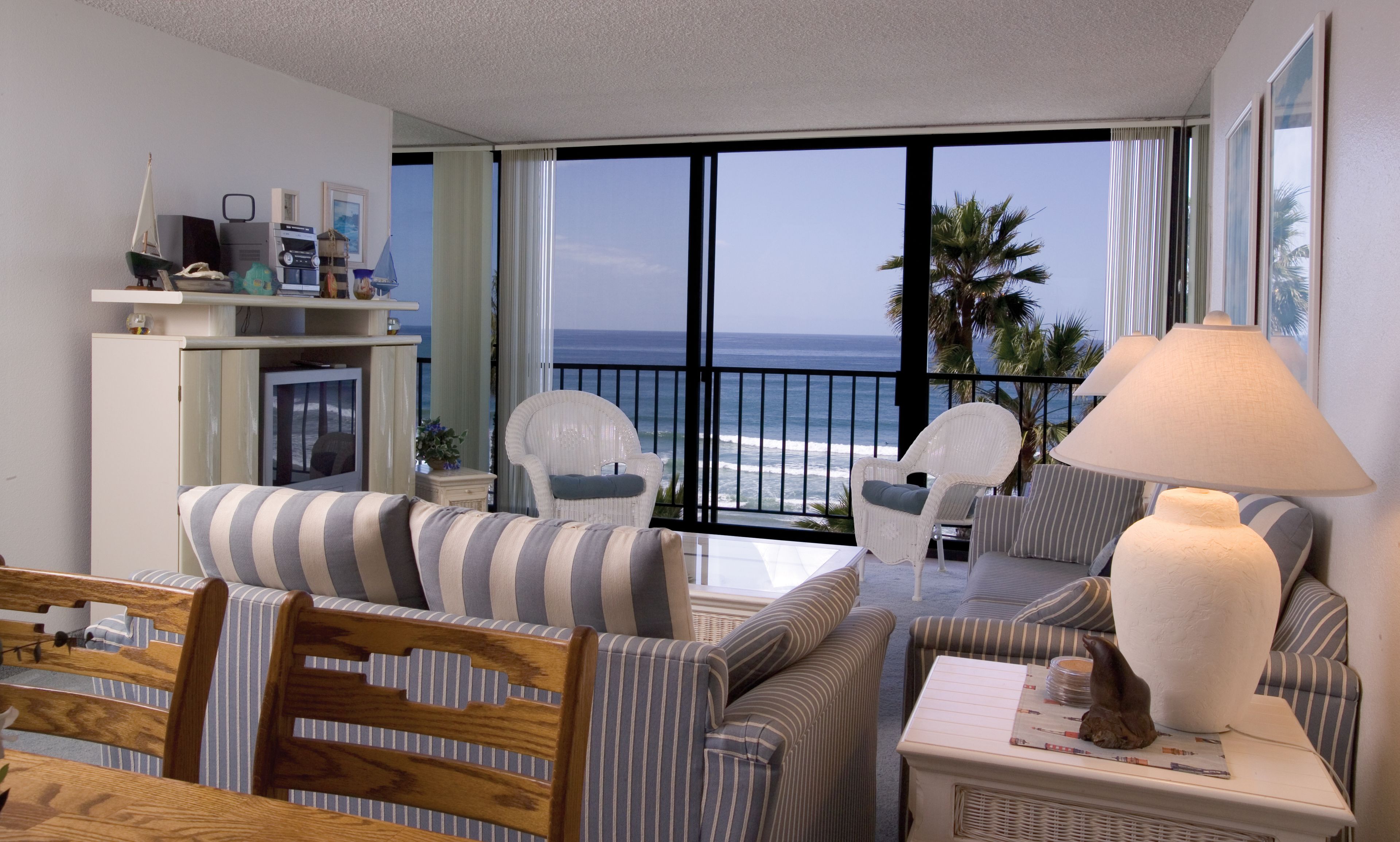 Varanda com vista para o oceano, mobiliada com sofás e cadeiras listrados, uma mesa e um abajur.