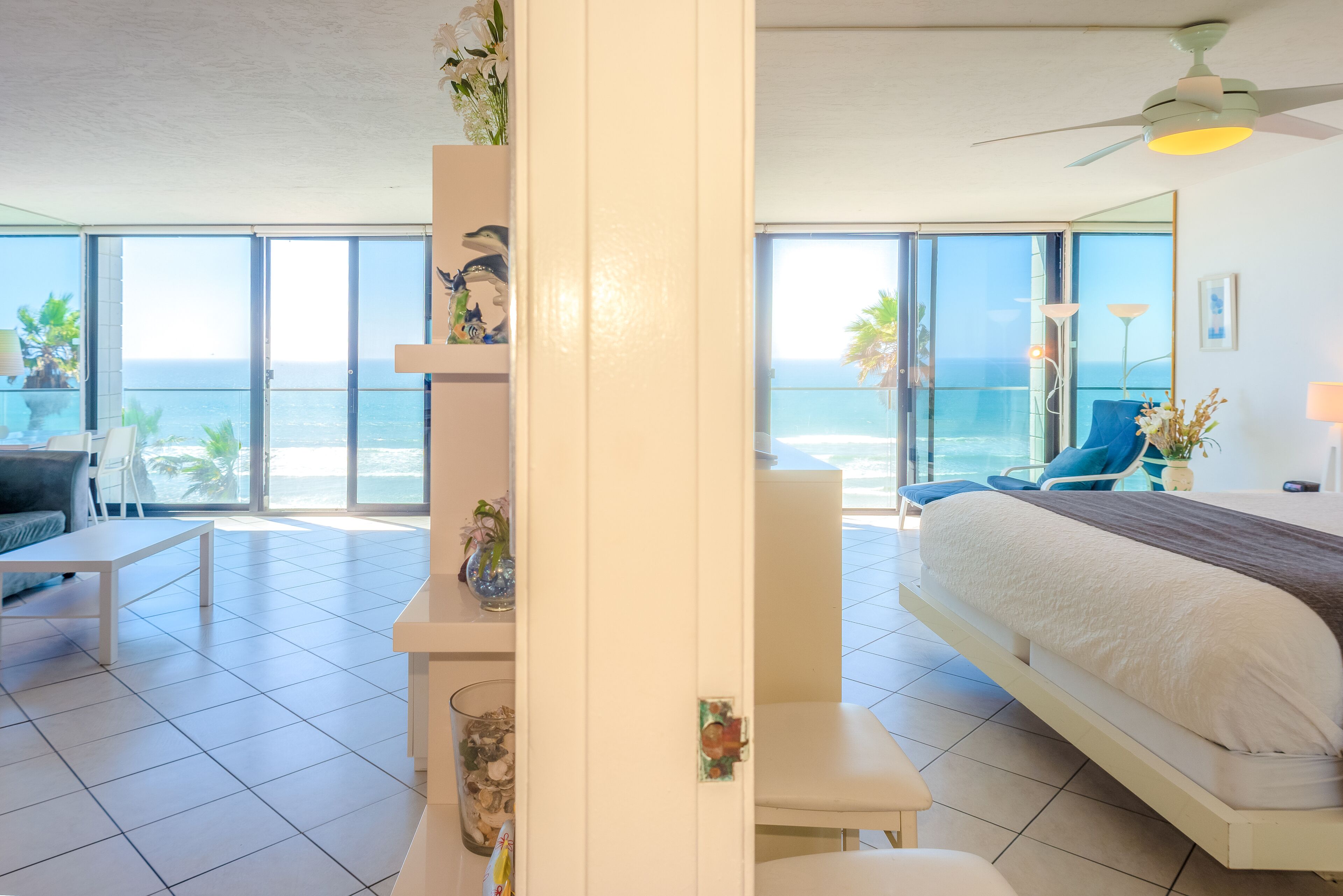 Een moderne hotelkamer met een groot bed, een zithoek met een tafel en stoelen, een balkon met uitzicht op de oceaan en een plafondventilator.