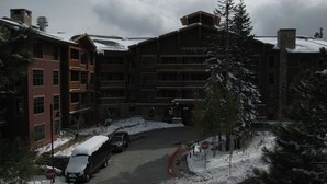 A multi-story building with a ski lodge entrance, snow-covered ground, and a parking area with vehicles. - Val d'Isere by Mammoth Reservation Bureau (Mammoth Lakes)