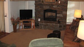 A living room with a stone fireplace, a television on a stand, a bookshelf, and a couch. - Val d'Isere by Mammoth Reservation Bureau (Mammoth Lakes)