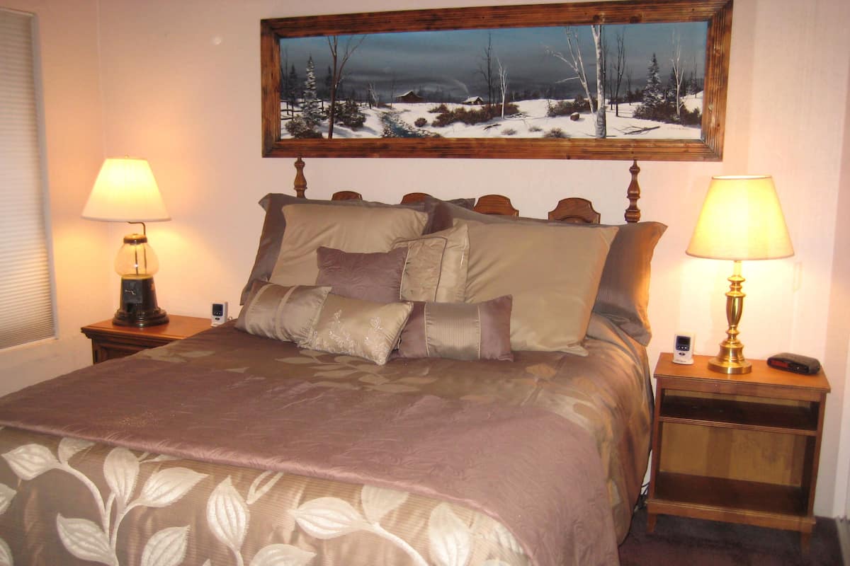 Ein ordentlich bezogenes Bett mit floralem Überwurf, zwei Nachttischlampen, ein Nachttisch mit einer Uhr und ein gerahmtes Bild über dem Bett.