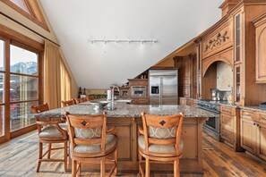 A spacious kitchen with a large island, wooden cabinets, and a view of mountains through the windows. - Faraway Jackson Hole (Teton Village)