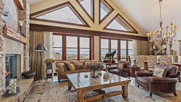 A spacious living room with a fireplace, large windows, and a chandelier.