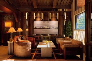 A cozy living room with a large flat-screen TV, leather sofas, a coffee table, and a stone wall. - Faraway Jackson Hole (Teton Village)