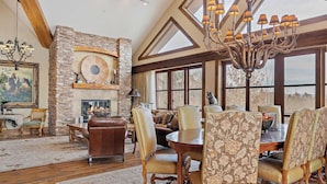 A spacious living room with a stone fireplace, a chandelier, and a large window offering a view. - Faraway Jackson Hole (Teton Village)