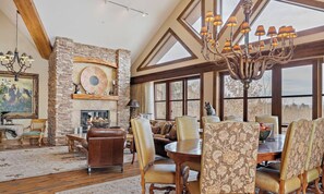 A spacious living room with a stone fireplace, a chandelier, and a large window offering a view. - Faraway Jackson Hole (Teton Village)