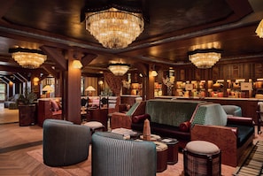 A lobby with multiple seating areas, chandeliers, and a bar area with various items. - Faraway Jackson Hole (Teton Village)