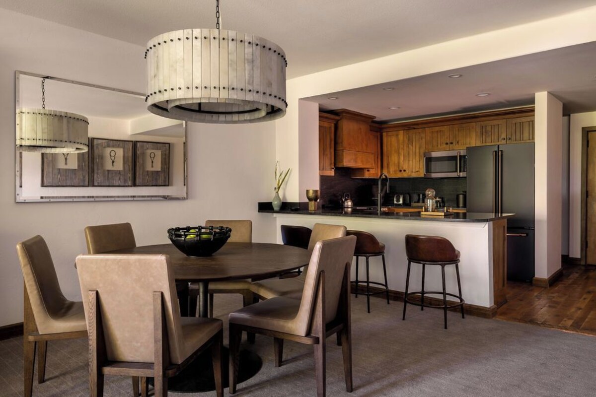 A modern kitchen with wooden cabinets, a central island, and a dining area with a round table and chairs.