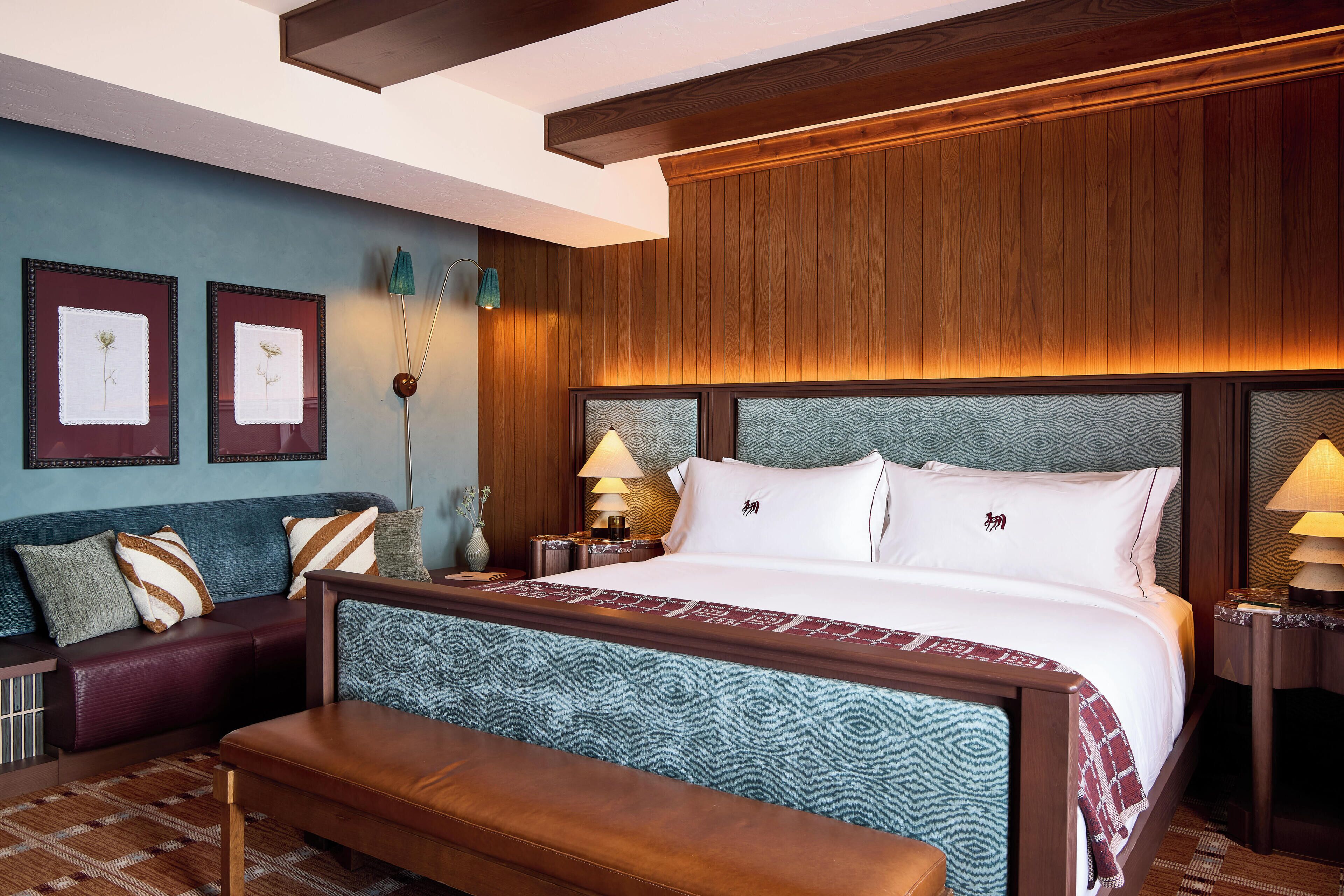 Een hotelkamer met een groot bed, een bankje, een sofa en ingelijste foto's aan de muur.