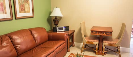 A brown leather sofa, a small table with a lamp, two wicker chairs, and a potted plant.