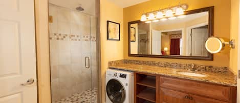 Un baño con lavadora y secadora integradas, un espejo grande y una ducha con puerta de cristal.