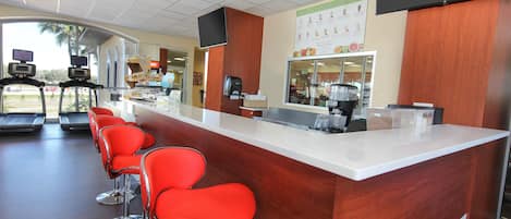 Un gimnasio moderno con una recepción, una estación de café y equipo de ejercicio.