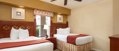 A hotel room with two beds, a ceiling fan, and a window with a view.