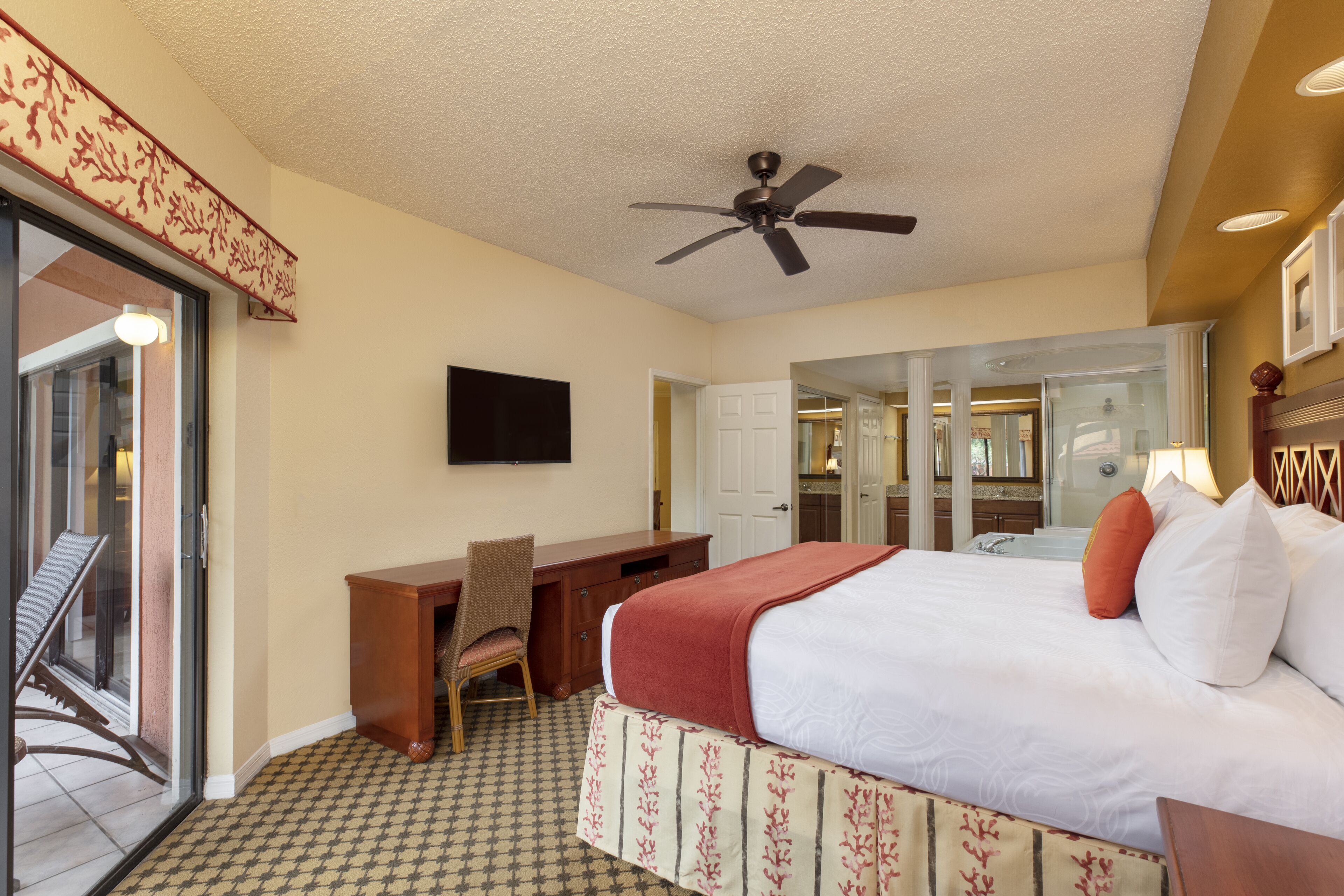 A hotel room with a bed, desk, chair, and a ceiling fan.
