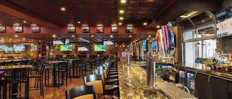 Un restaurant doté de nombreuses tables et chaises, d’un bar avec un comptoir et des tabourets, et de plusieurs téléviseurs fixés aux murs.