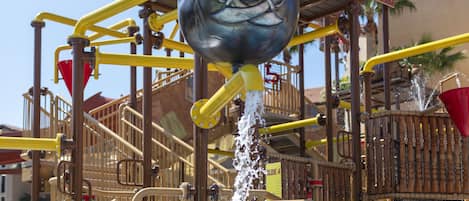A water play area with a pirate-themed structure, including a ship's wheel and a flag.