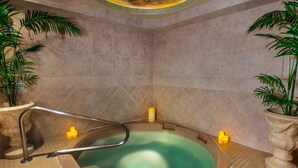 A hot tub with a metal ladder, surrounded by beige tiles and potted plants.