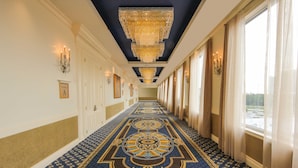 A hallway with a patterned carpet, chandeliers, and framed pictures on the walls.