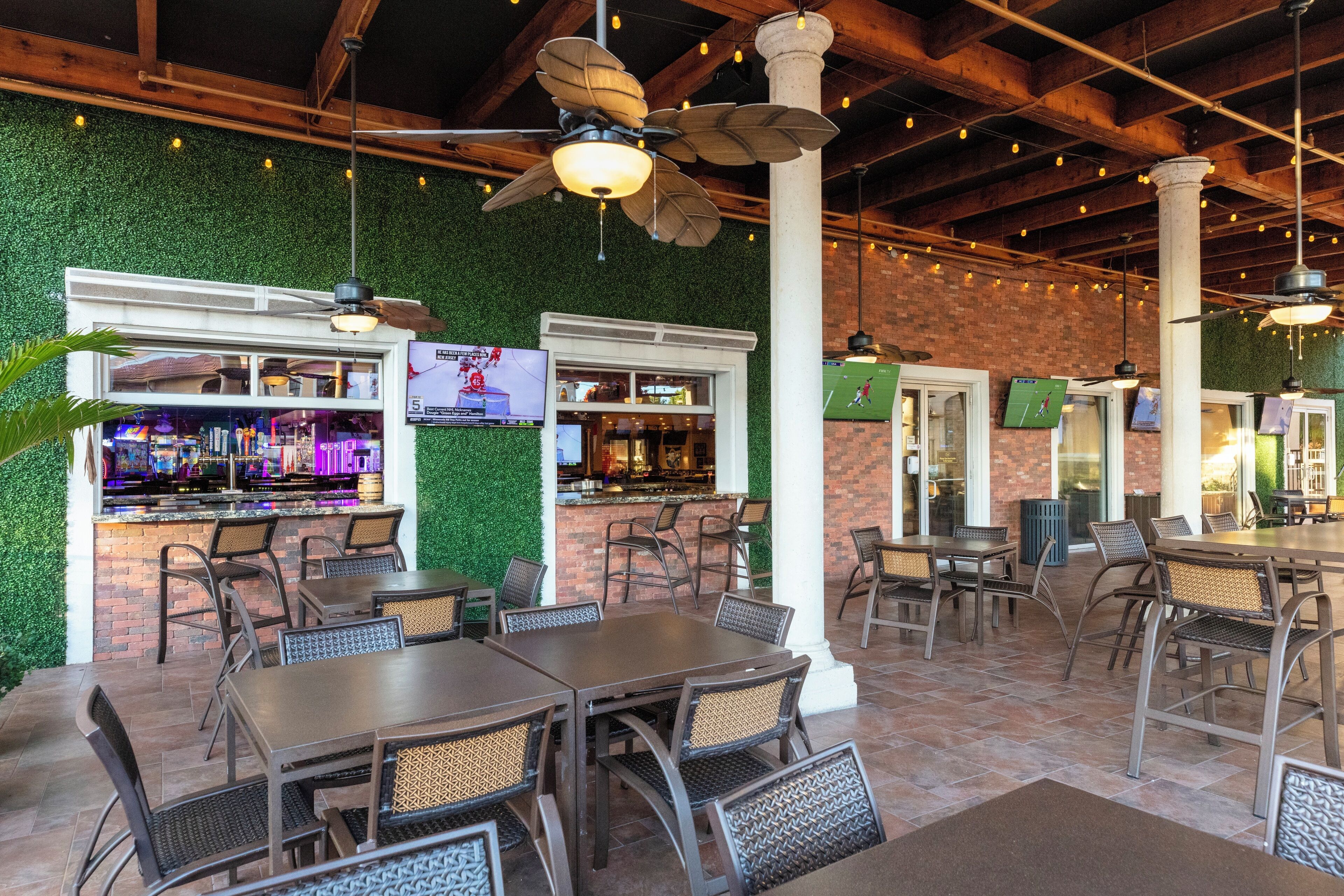 An outdoor dining area with brick walls, green foliage, and wooden tables and chairs.