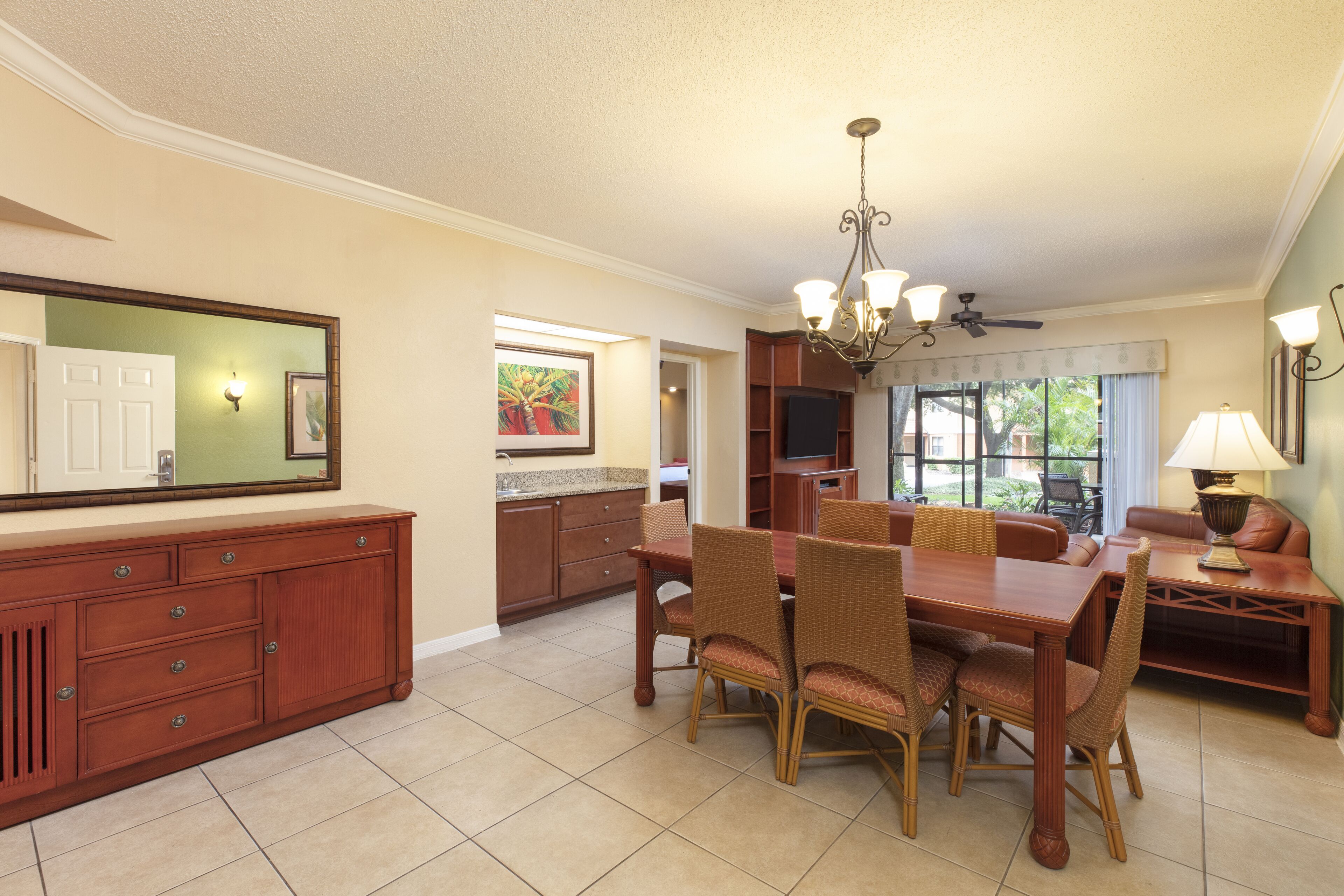 A dining area with a wooden table and chairs, a chandelier, and a television in the background.