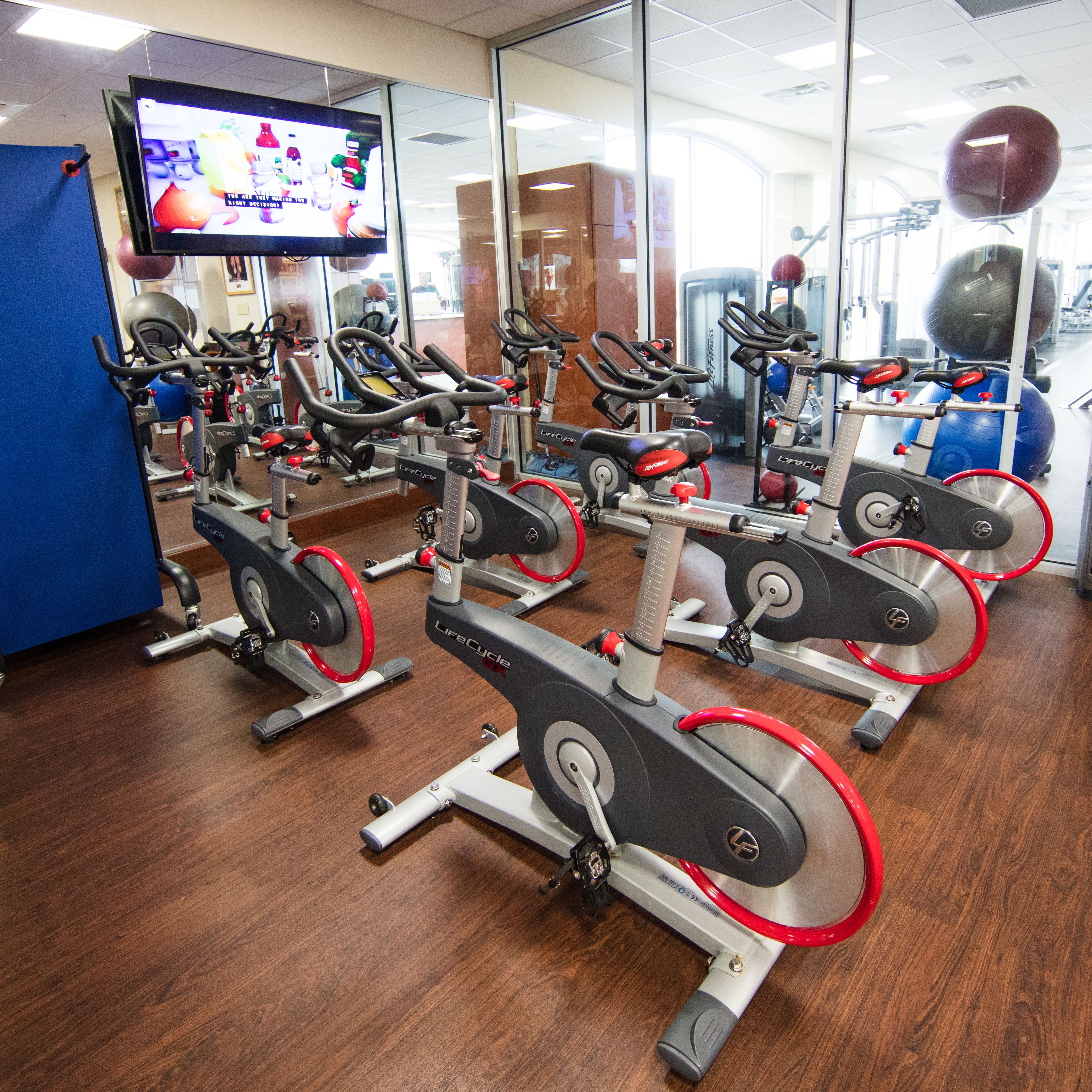 A gym with multiple stationary bikes, a television screen, and exercise balls.