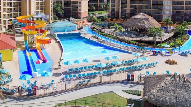 A resort with a large pool, a water slide, and multiple buildings with balconies.