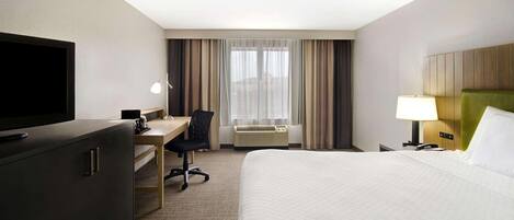Quarto de hotel com cama, escrivaninha, cadeira, televisão, abajur e ar condicionado.