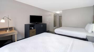 A hotel room with two beds, a desk with a lamp, a television, and a wardrobe.