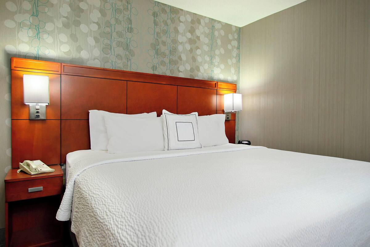 Ein Hotelzimmer mit einem großen Bett, zwei Nachttischlampen, einem Nachttisch mit Telefon und einer Wand mit Blumenmuster.