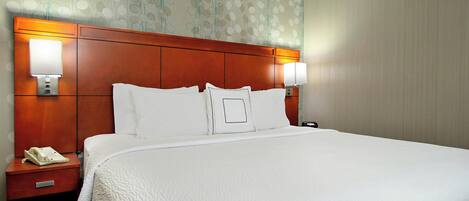 A hotel room with a large bed, two bedside lamps, a nightstand with a telephone, and a wall with a floral pattern.