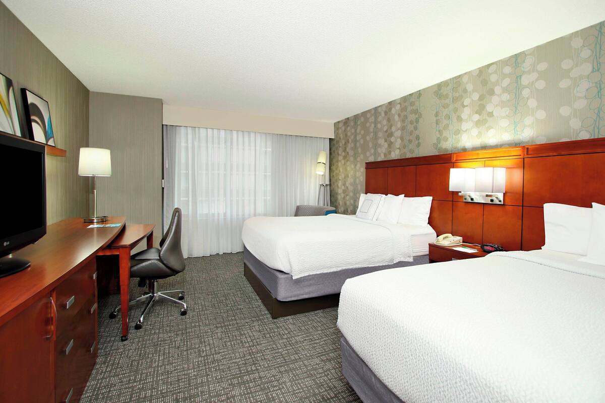 Ein Hotelzimmer mit zwei Betten, einem Schreibtisch, einem Fernseher, einem Sessel und einer Lampe.