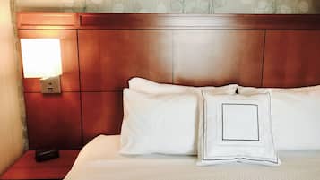 Una habitación de hotel con cabecera de madera, una mesita de noche con control remoto y una cama con ropa blanca y almohadas.