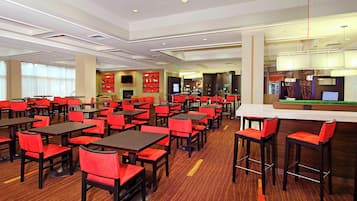 A spacious dining area with multiple tables and red chairs, a bar area with stools, and a modern ceiling design.