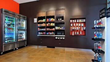 A modern retail space with refrigerated beverage dispensers, shelves stocked with snacks and beverages, and a microwave.