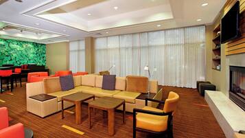 A modern hotel lobby with a sectional sofa, armchairs, a coffee table, a piano, and a TV mounted on the wall.