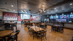 A spacious restaurant with multiple tables and chairs, a bar area, and a large screen displaying sports content. - Coast Nisku Inn & Conference Centre (Nisku)