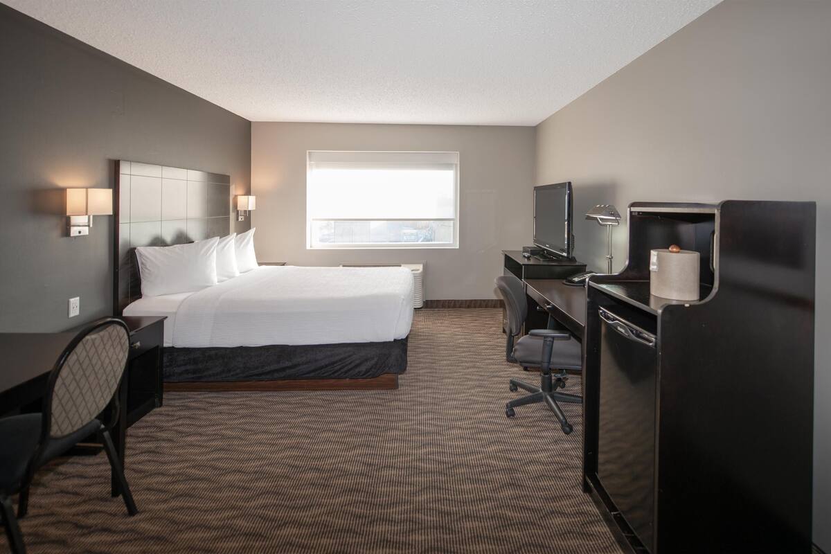 A hotel room with a bed, desk, chair, television, and a window.