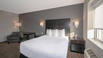 Une chambre d’hôtel avec un grand lit, deux tables de chevet avec des lampes, un bureau avec une chaise et une fenêtre avec des stores.
