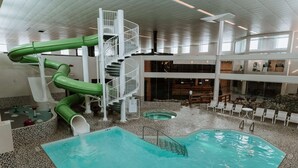 A large indoor swimming pool with a green slide, a staircase, and lounge chairs. - Coast Nisku Inn & Conference Centre (Nisku)