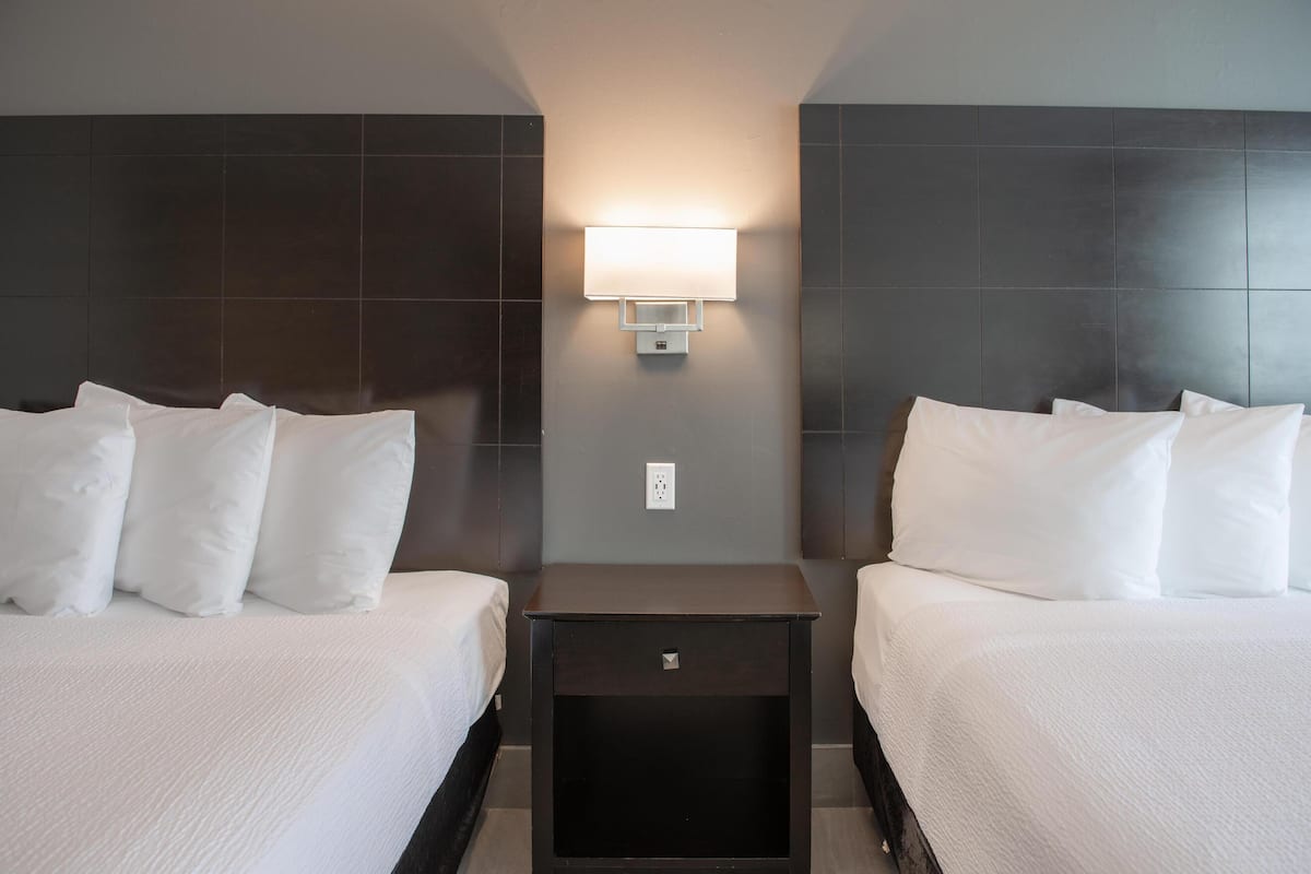 A hotel room with two beds, a nightstand, and a wall-mounted light fixture.
