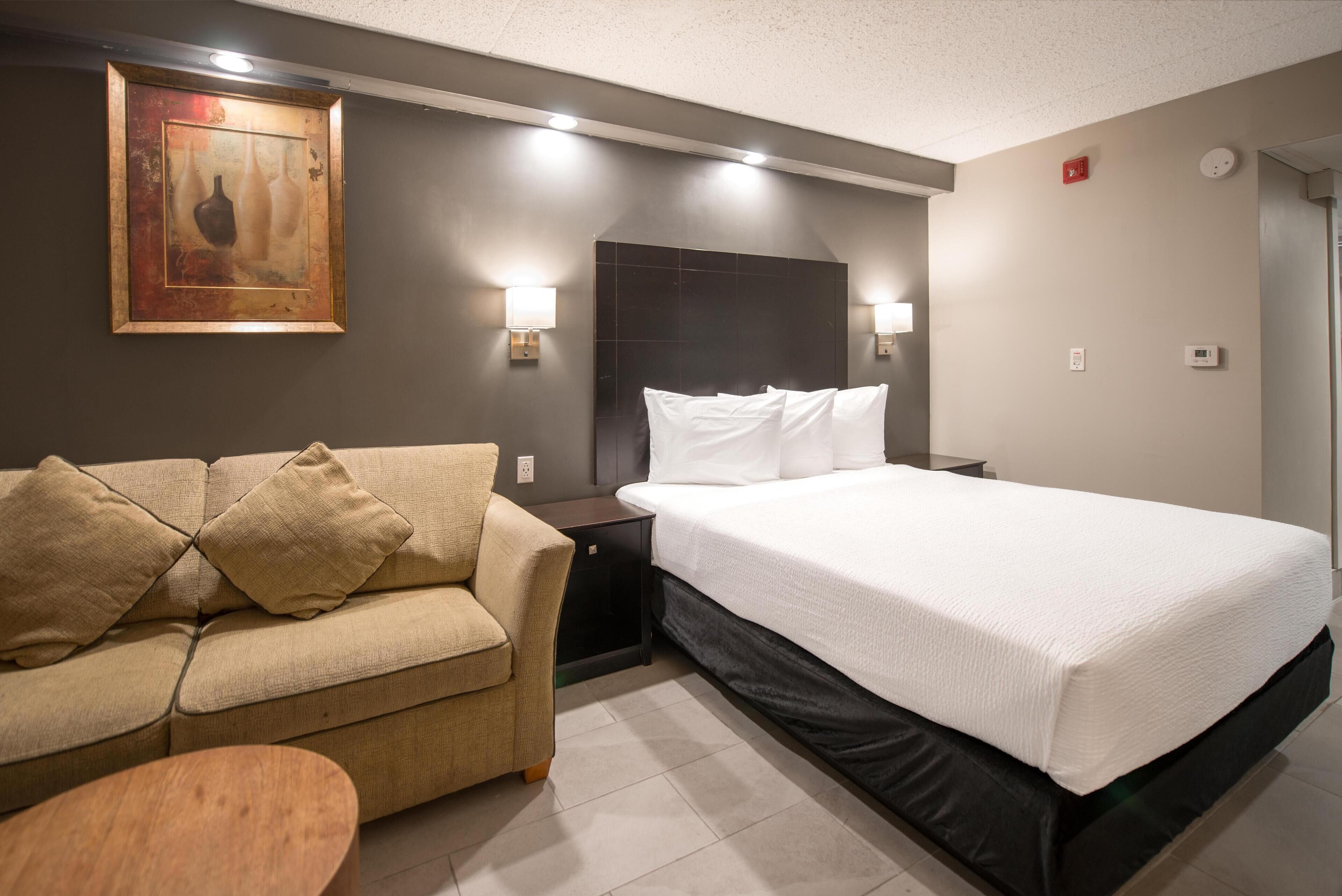 Quarto de hotel com cama, sofá, mesa de cabeceira e pintura pendurada na parede.