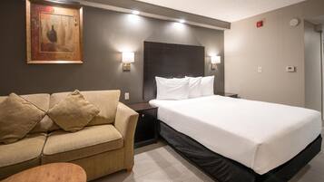 Quarto de hotel com cama, sofá, mesa de cabeceira e pintura pendurada na parede.
