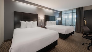 A hotel room with two beds, a desk, a chair, and a large window with curtains. - Coast Nisku Inn & Conference Centre (Nisku)