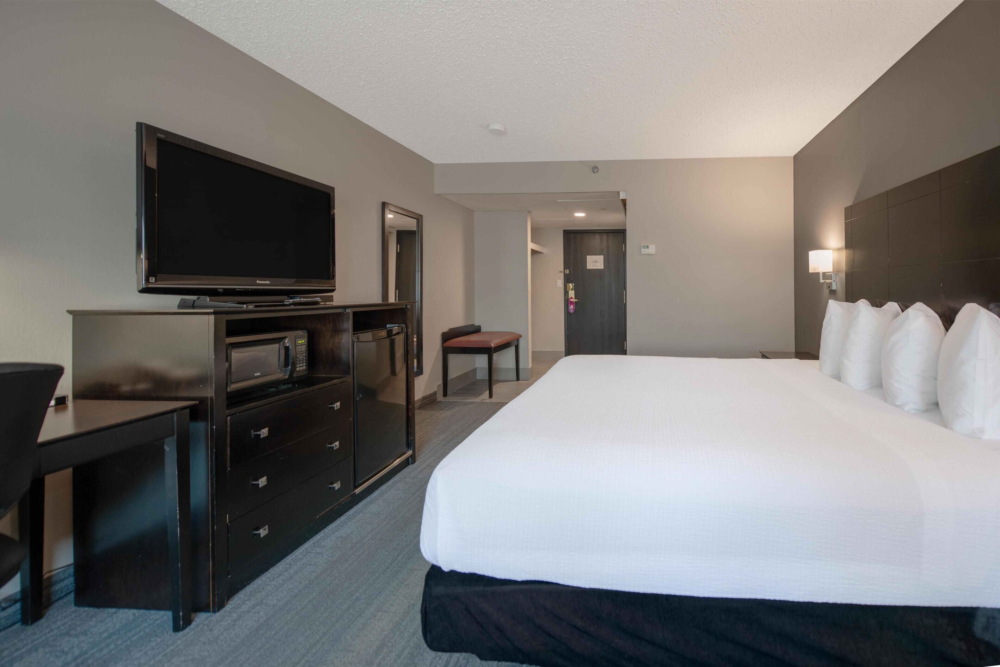 A hotel room with a large bed, a flat-screen TV, a desk, a microwave, and a chair.