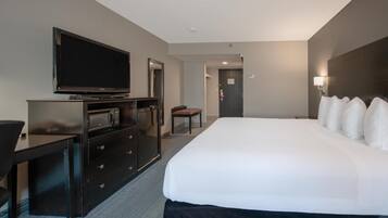 A hotel room with a large bed, a flat-screen TV, a desk, a microwave, and a chair.