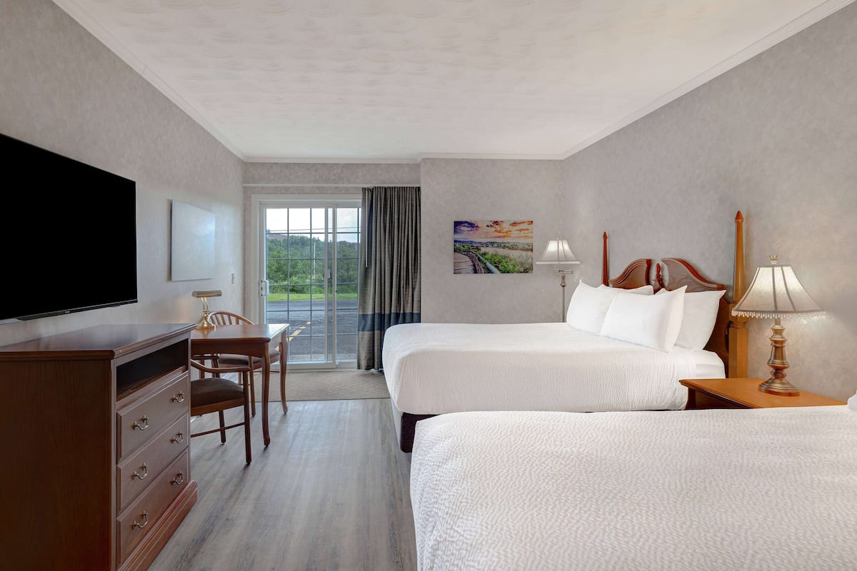 Habitación de hotel con dos camas, televisión, escritorio y vista a zonas verdes por la ventana.