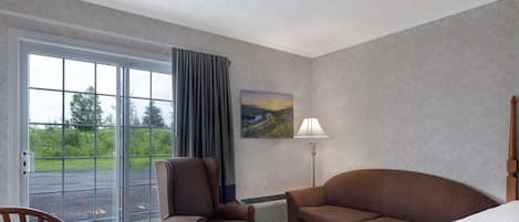 A hotel room with a large sliding glass door, a brown armchair, a brown sofa, a wooden table, and a white bed.