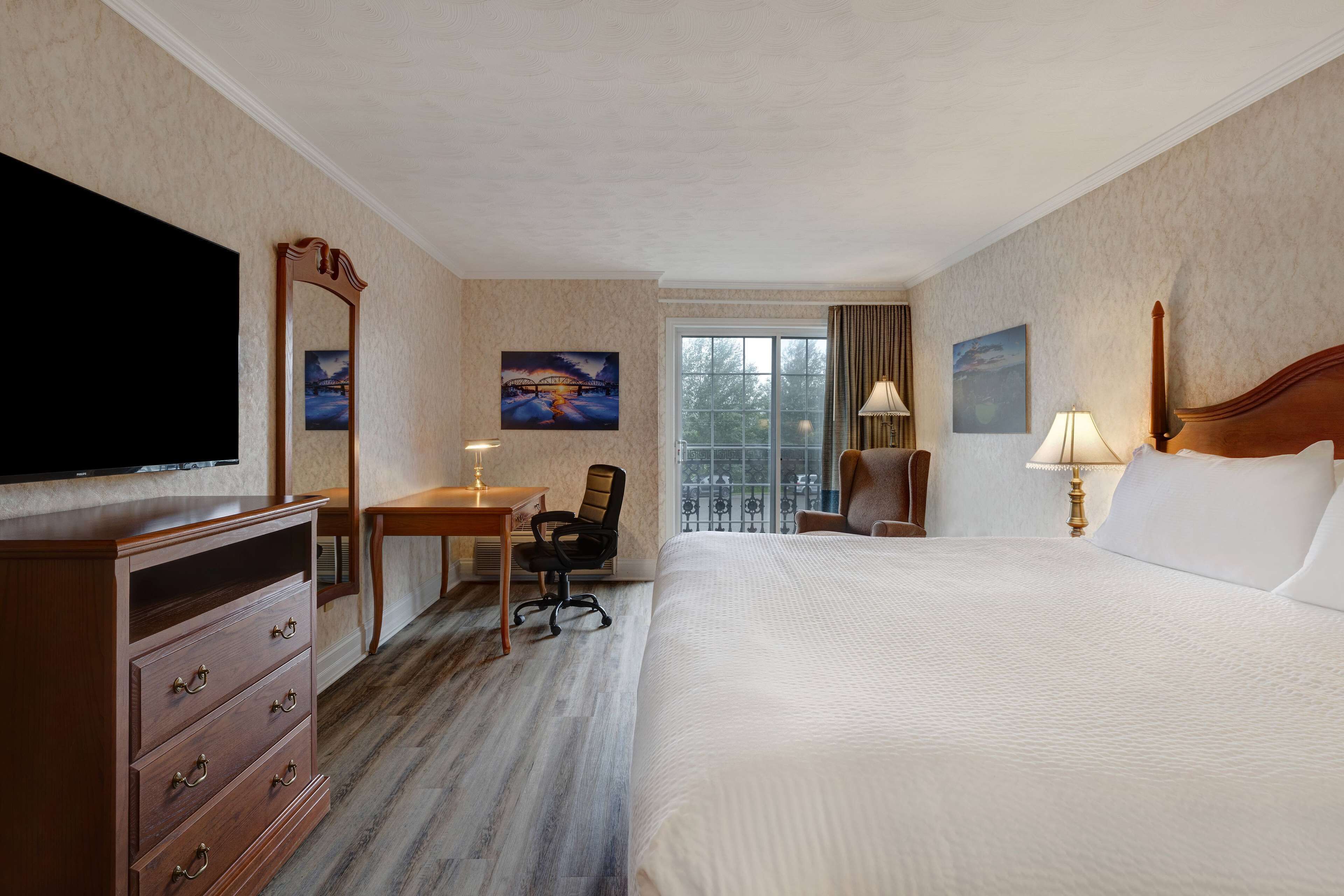 Una camera d'hotel con un letto grande, una scrivania con una sedia, una televisione e opere d'arte alle pareti.
